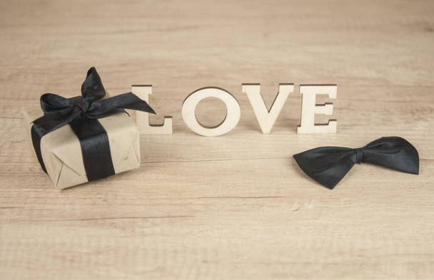 деревянное слово ЛЮБОВЬ с бабочкой галстук и подарочная коробка на деревянный стол. С Днем Святого Валентина - Фото, изображение