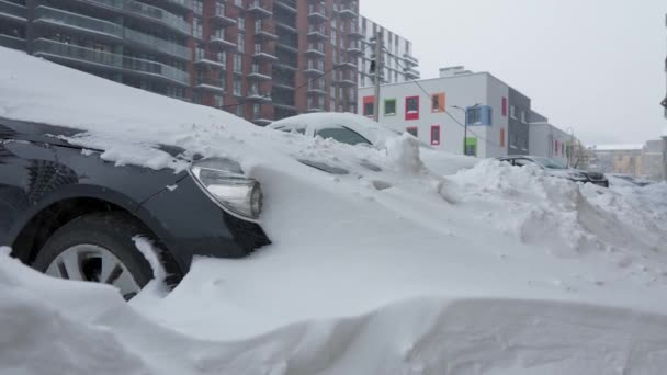 Auto 's bedekt met sneeuw na een sneeuwstorm. Woningbouw op de achtergrond. - Video