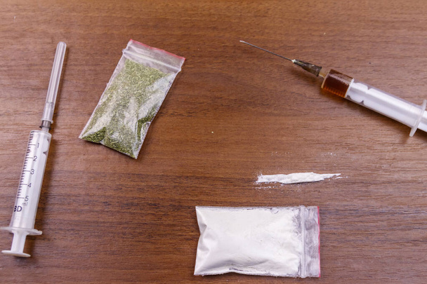 Různé druhy drog: kokain, heroinová stříkačka a sušené konopí na stole. Koncept užívání drog, kriminality a závislosti - Fotografie, Obrázek