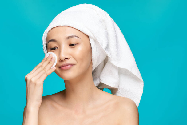 bonita mujer limpiándose la cara con una almohadilla de algodón piel limpia salud fondo azul - Foto, Imagen