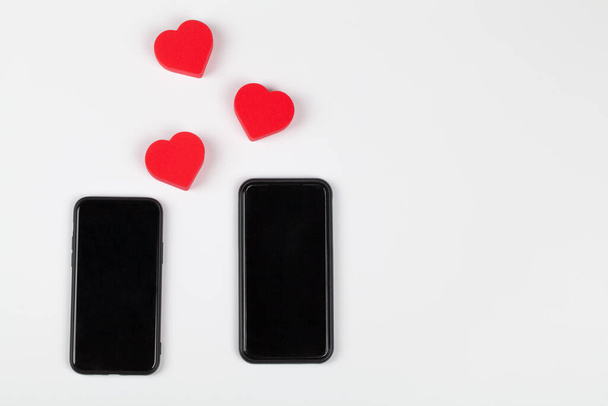 Красные сердца и два мобильных телефона на белом фоне. Интернет знакомства, копировальное пространство - Фото, изображение