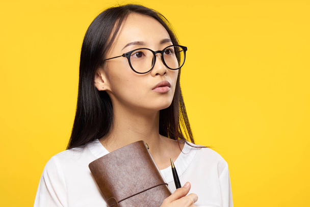 ázsiai nő szemüveges jegyzettömb tollal a kezében iroda menedzser sárga háttér - Fotó, kép