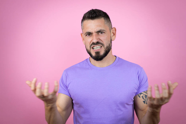 Joven hombre guapo con camiseta casual sobre fondo rosa loco y loco gritando y gritando con expresión agresiva y los brazos levantados. Concepto de frustración. - Foto, imagen