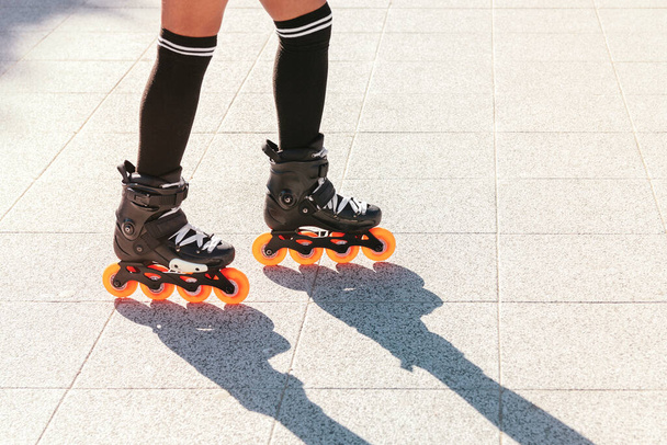 Gros plan des jambes d'une femme patinant avec des patins à roues alignées à l'extérieur par une journée d'été chaude et très ensoleillée. L'ombre est projetée sur le sol en pierre. Espace de copie - Photo, image