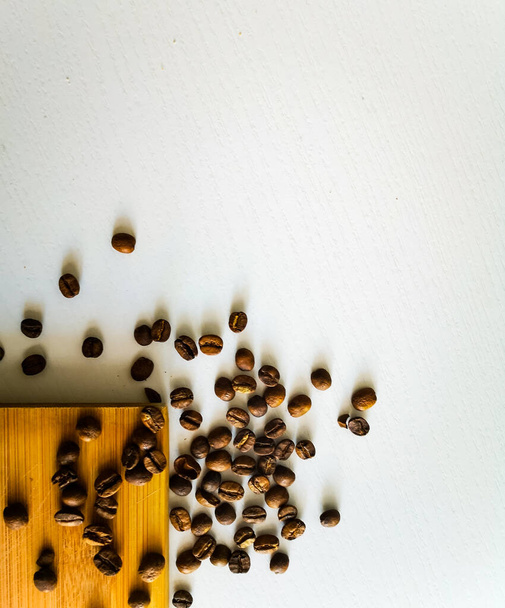 Koffiebonen liggen op houten plank en witte tafel - Foto, afbeelding