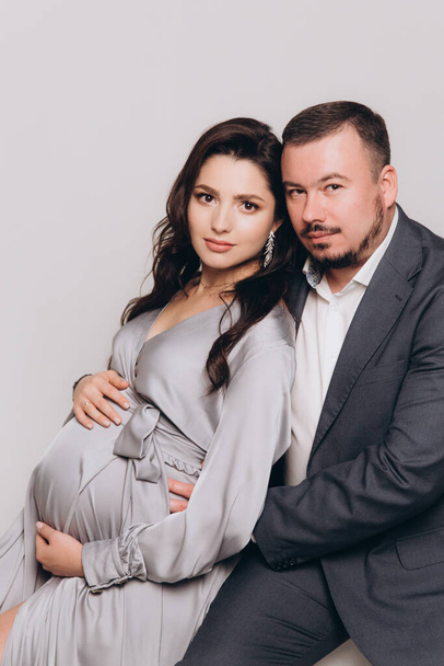 Pregnancy photoshoot of a beautiful couple, future parents in a gray dress and suit - Photo, Image