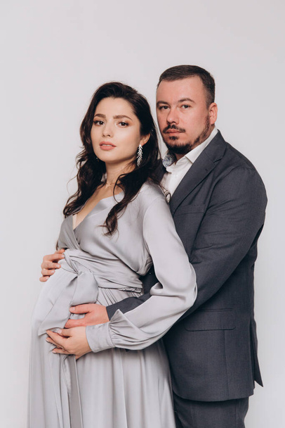 Pregnancy photoshoot of a beautiful couple, future parents in a gray dress and suit - Photo, image