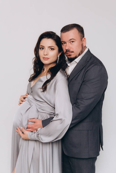 Pregnancy photoshoot of a beautiful couple, future parents in a gray dress and suit - Fotó, kép