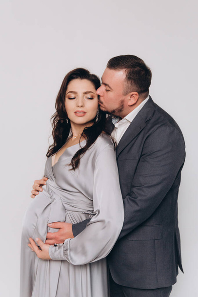 Pregnancy photoshoot of a beautiful couple, future parents in a gray dress and suit - Фото, изображение