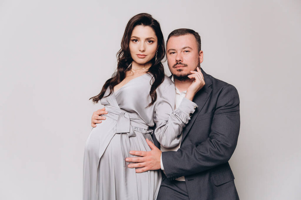 Pregnancy photoshoot of a beautiful couple, future parents in a gray dress and suit - Foto, immagini