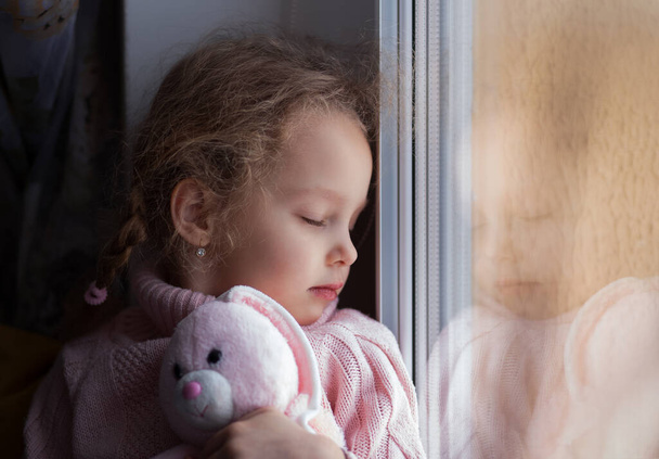 Una niña se sienta y mira por la ventana. Pensativo. - Foto, Imagen