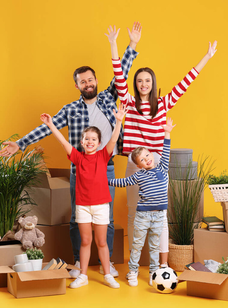 Delighted parents and kids having fun and raising arms while standing together among boxes with belongings after relocation into new apartment - Foto, afbeelding