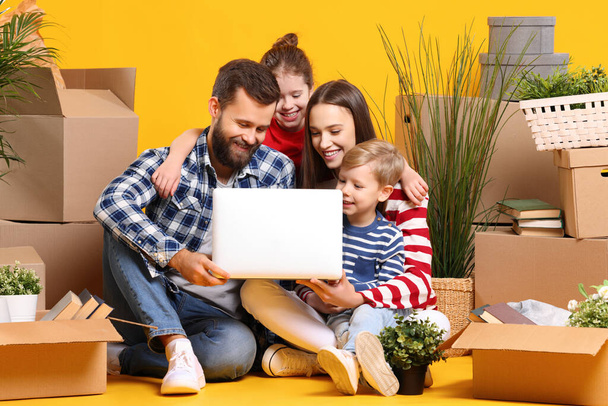 Smiled happy family: parents and kids browsing laptop and searching for new house while sitting together among boxes with stuff - Photo, Image