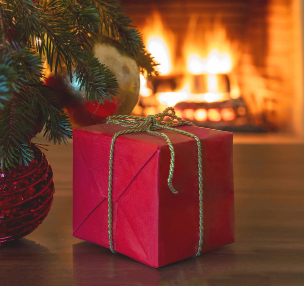 Noël intérieur concept de célébration de la maison. Vue rapprochée de la branche d'arbre de Noël avec des boules, une boîte cadeau avec ruban doré et fond de cheminée flou. Des moments chauds en famille. - Photo, image