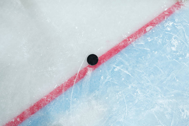 Puck sdraiato sulla linea rossa che divide lo spazio di gioco e la zona di rete sulla pista di ghiaccio per giocare a hockey che può essere utilizzato come sfondo - Foto, immagini