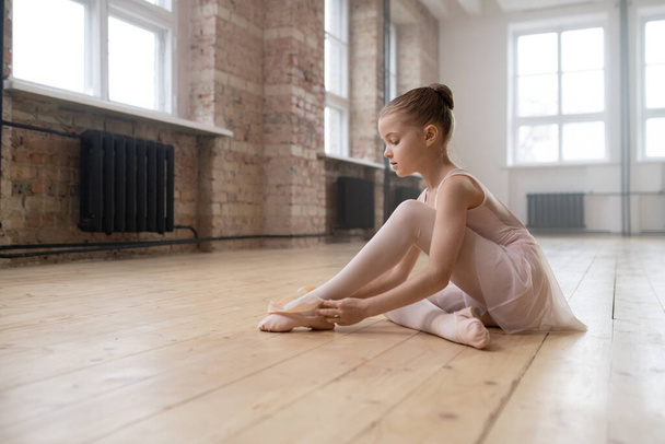ダンススタジオの床に座っている小さなバレリーナの女の子と置きますザ · ポイントシューズ前にクラス - 写真・画像