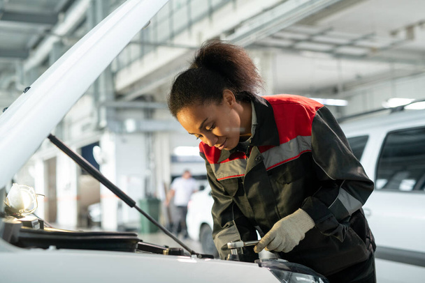 Fiatal női munkavállaló autójavítási szolgáltatás fölé hajló nyitott motortér, és keresi az oka a hiba a műhelyben - Fotó, kép