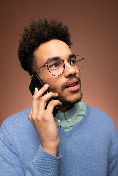 Mladý smíšeného-závod podnikatel v brýlích a chytré ležérní oblečení drží smartphone za ucho během obchodního hovoru - Fotografie, Obrázek