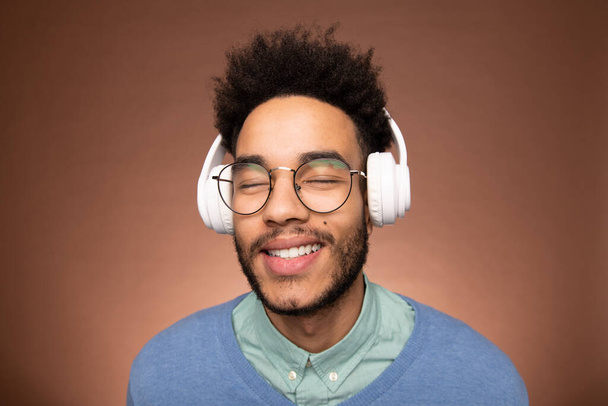 眼鏡とスマートカジュアルウェアの幸せな若い混合レースのビジネスマンは、ヘッドフォンで音楽を楽しみながら彼の目を閉じて - 写真・画像