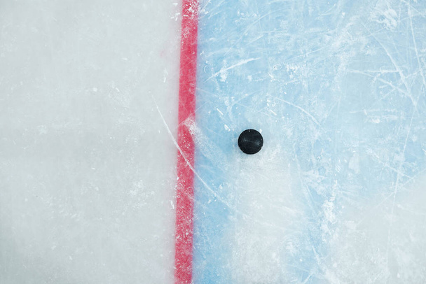Black puck lying by red line on ice rink for playing hockey on stadium that can be used as background for sports advertisement or announcement - Photo, Image