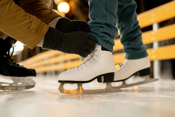 Primer plano del hombre ayudando a su novia a atar cordones en patines de figuras antes de patinar - Foto, Imagen