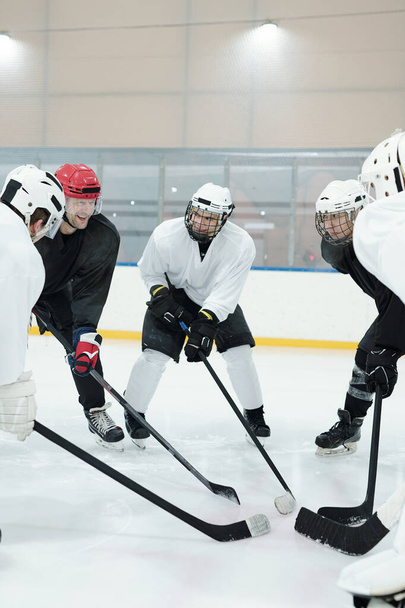 Skupina profesionálních hokejistů ve sportovní uniformě, ochranných přilbách, rukavicích a bruslích stojící v kruhu na kluzišti během tréninku před hrou - Fotografie, Obrázek