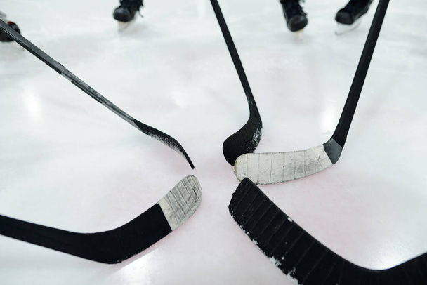 Group of hockey sticks in the middle of circle made up of several players standing on ice rink and training while preparing for play - Photo, Image