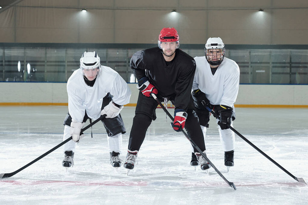 Drei Eishockeyprofis in Uniform, Handschuhen, Schlittschuhen und Helmen, die sich beim Training vor dem Spiel auf der Eisfläche nach vorne beugen - Foto, Bild