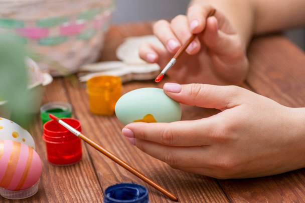 A woman with a tassel paints Easter eggs. Preparing decorations for Easter, creativity with children, traditional symbols. Preparing for Easter. - Photo, image