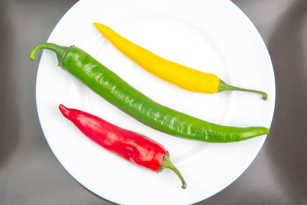 chili chaud jaune, rouge et vert sur une assiette. Du poivre. Aliments vitaminés végétaux. - Photo, image