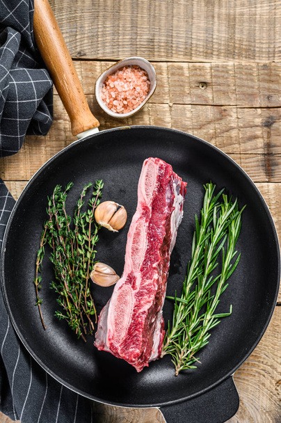 Carne cruda fresca di costole corte di manzo su una pentola con erbe. sfondo in legno. Vista dall'alto - Foto, immagini