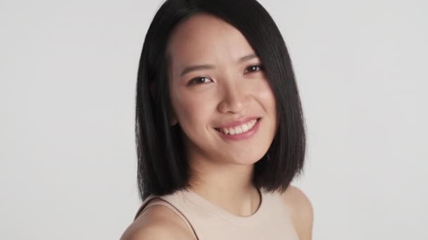 Close up bela menina asiática olhando encantador sorrindo na câmera sobre fundo branco. Jovem mulher bonita posando em estúdio - Filmagem, Vídeo
