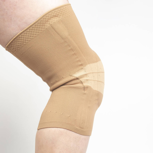 bendaggio per fissare il ginocchio ferito della gamba umana su uno sfondo bianco. medicina e sport. trattamento delle lesioni agli arti - Foto, immagini