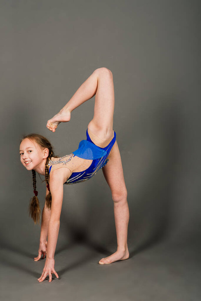 Молода дівчина займається гімнастикою на сірому фоні, студія
 - Фото, зображення