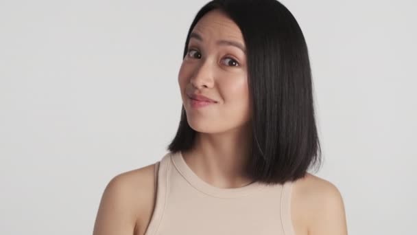 Mladá atraktivní asijská žena vypadá nadšeně přes bílé pozadí. Dívka překvapivě dívá do kamery - Záběry, video