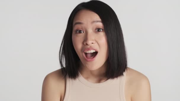 Beautiful amazed Asian girl rejoicing because of good news on camera over white background. Wow expression - Footage, Video