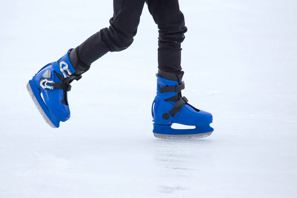 Τα πόδια ενός άντρα με μπλε πατίνια οδηγούν σε παγοδρόμιο. χόμπι και αναψυχή. χειμερινά αθλήματα - Φωτογραφία, εικόνα