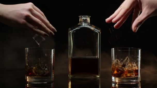 Bir bardak konyaklı viski ve buz küplü iki el siyah arka planda tezahürat yapıyor. - Video, Çekim