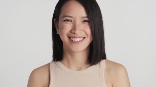 Портрет очаровательной азиатской девушки, выглядящей счастливой, гордящейся на белом фоне. Женщина в помещении - Кадры, видео