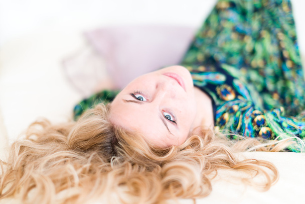 Beautiful young blonde woman with long hair smiling and lying - 写真・画像