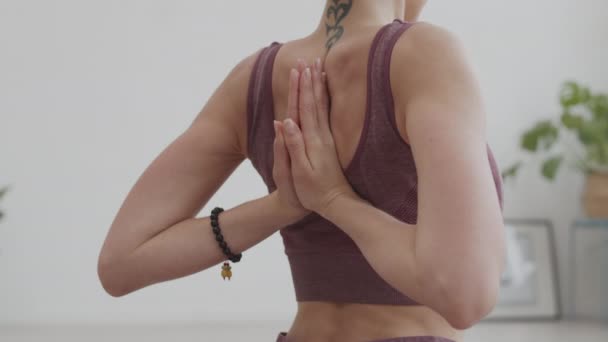 Vista trasera de yogui femenino irreconocible usando ropa deportiva haciendo pose con las manos detrás de la espalda durante la práctica de yoga en interiores - Imágenes, Vídeo