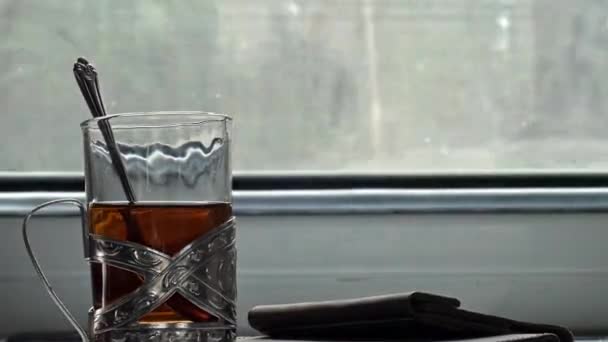 Oekraïense spoorwegen. Op de tafel in het compartiment staat thee in een traditionele bekerhouder. Close-up van een hand die een theezakje uit een glas haalt. Thee zetten. Reis. - Video