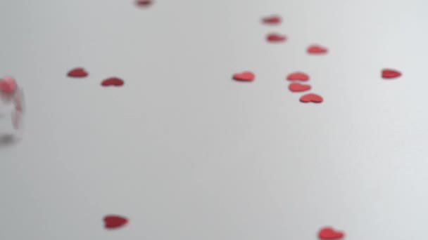 Concept video achtergrond voor Valentijnsdag Veel rood glanzende hart vormige confetti vallen op de tafel.Close-up video van vallende sprankelende harten. 4K. - Video
