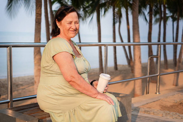 ウォーターフロントの高齢者の女性の肖像画。海を背景にベンチに座って引退 - 写真・画像