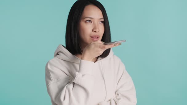 Vonzó ázsiai lány rögzíti a hangüzenetet, hogy barátja segítségével okostelefon elszigetelt kék háttérrel. Távolsági kommunikáció - Felvétel, videó