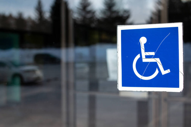 Ikona International Symbol of Access, niebieski kwadrat z białym graficznym wózkiem i osobą, w oknie w Londynie Ontario Kanada, luty 2021.   - Zdjęcie, obraz