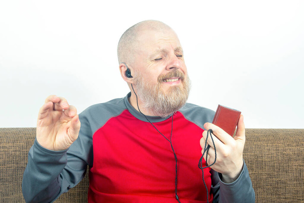 γενειοφόρος άνθρωπος απολαμβάνει να ακούει την αγαπημένη του μουσική μέσω ενός ακουστικού σε μικρά ακουστικά. ακουστόφιλος και λάτρης της μουσικής. μουσική και hi-fi ήχος. - Φωτογραφία, εικόνα