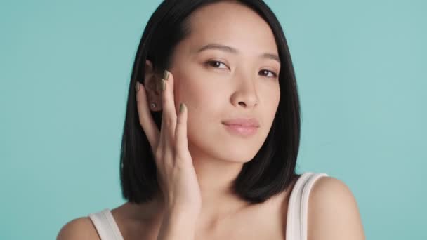 Gyönyörű ázsiai lány mutatja a kamera friss tiszta arc néz boldog elszigetelt kék háttér - Felvétel, videó