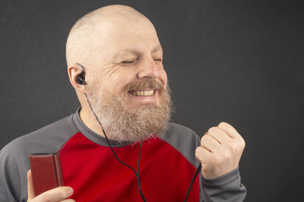 бородатый человек любит слушать свою любимую музыку через аудиоплеер в маленьких наушниках. аудиофил и любитель музыки. музыка и hi-fi звук. - Фото, изображение
