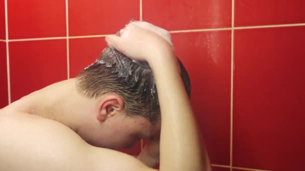 Młody mężczyzna pod prysznicem. Nastolatek myje się pod strumieniem ciepłej wody w łazience. - Materiał filmowy, wideo